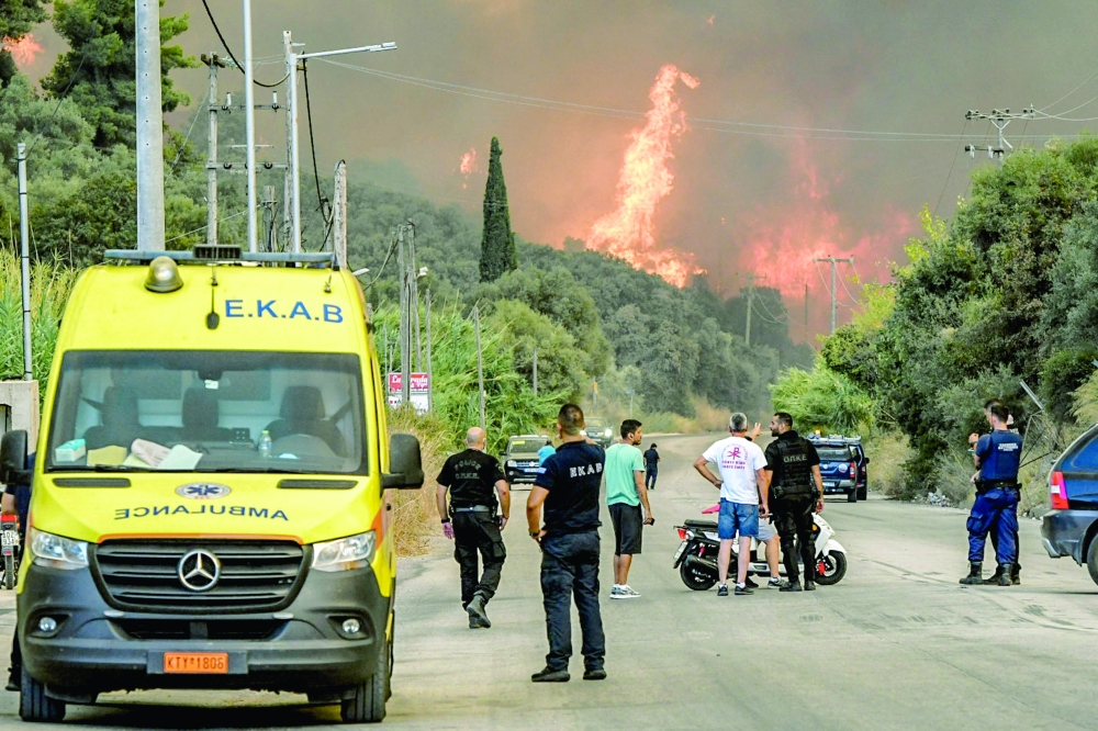 People stand on a road as a wildfire burns a forest near the city of Patras, Greece. — AFP