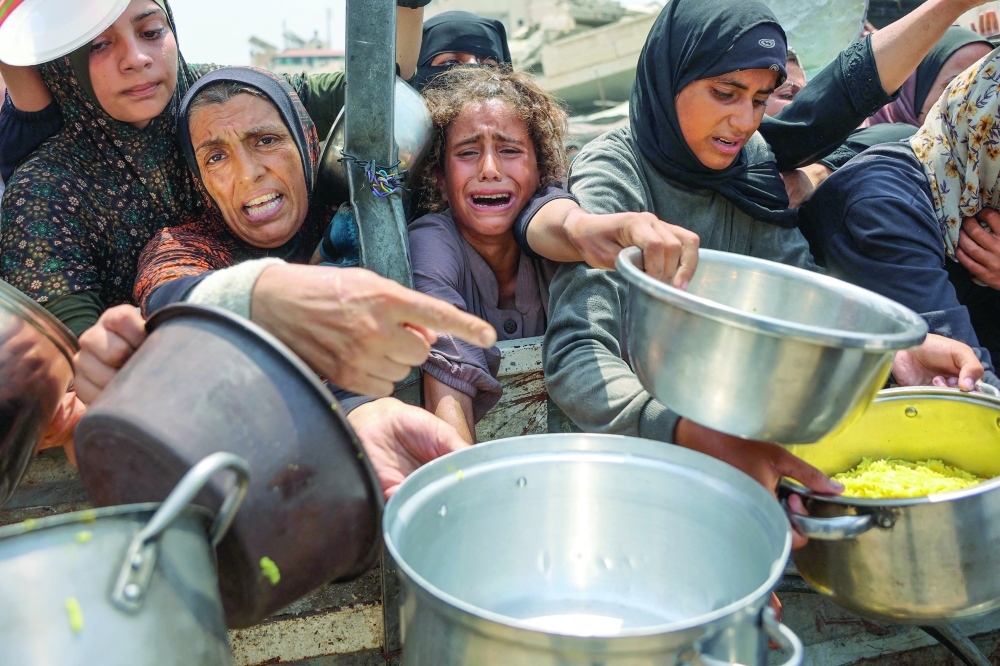 A Palestinian girl cries as she tries to receive cooked meals along with others, in Gaza. — AFP
