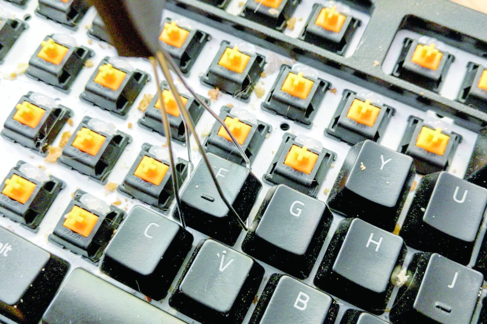 Use a wire keycap puller to carefully remove the keycaps by hooking the tool around the edges of each keycap and gently pulling straight up