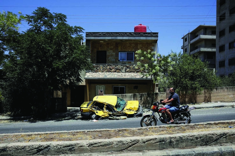 A man rides a motorcycle past a destroyed car, following deadly clashes in Sweida. — Reuters