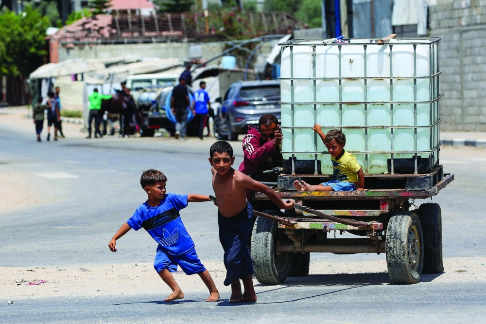 A man and young children push a cart carrying a water tank at the Bureij camp. — AFP
