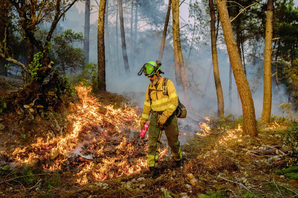 A firefighter walks through flames near San Martino de Alvaredos, Spain. — Reuters