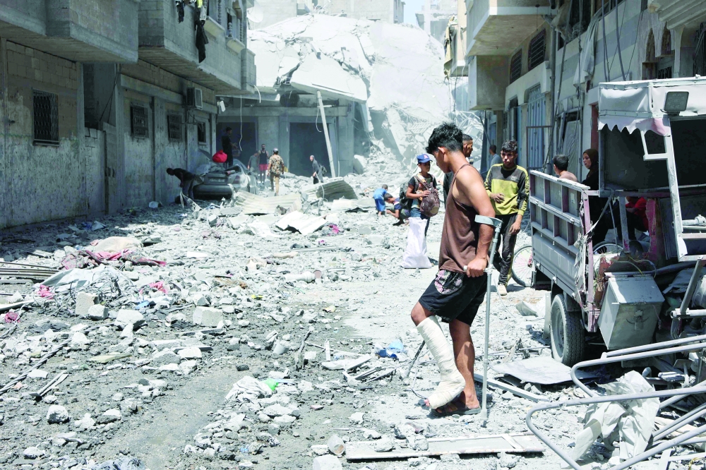 
An injured youth walks on debris as Palestinians salvage items from the rubble of homes destroyed in
Israeli strikes on the southern Al Zeitoun neighbourhood in Gaza City on Tuesday. — AFP 