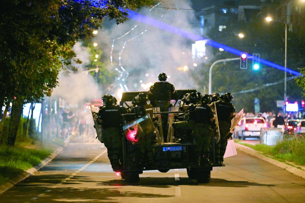 Serbian riot police officers travel on the back of a vehicle as they face protesters, in Belgrade. — AFP