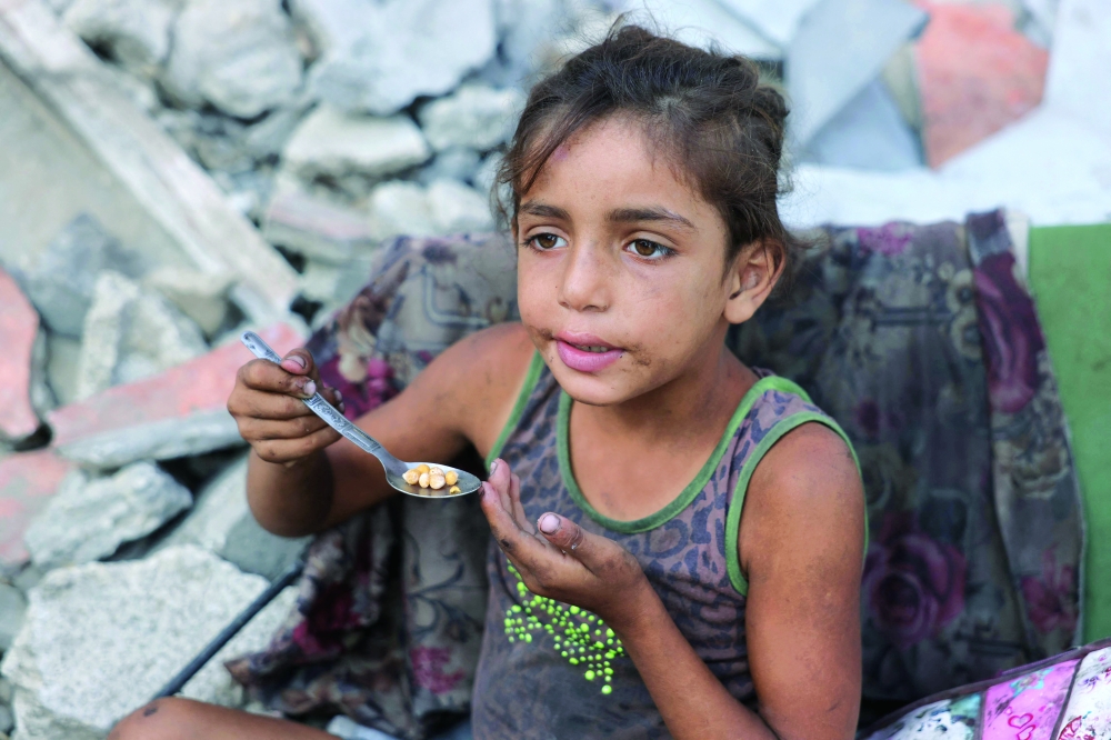 
A displaced Palestinian girl eats chickpeas as she sits amid the destruction in Saftawi neighbourhood, west of Jabalia in the northern Gaza Strip, on Sunday. — AFP 