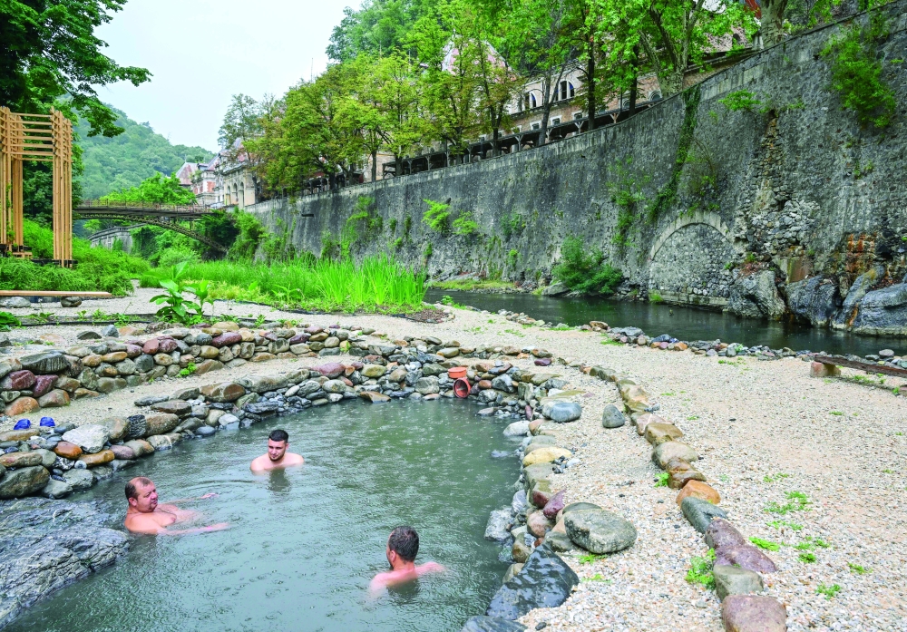 Tourist enjoy sulfurous thermal water in landscaped swimming pools restored by a group of young architects led by  Oana Chirila, next to Cerna riverbed in Baile Herculane on July 29, 2025. With graffiti now covering the crumbling walls of the main thermal baths in one of Europe's oldest spa towns, a group of young architects hopes to restore the picturesque Romanian resort that once attracted emperors after decades of neglect and corruption.
 - TO GO WITH AFP STORY by Ani SANDU
 (Photo by Daniel MIHAILESCU / AFP) / TO GO WITH AFP STORY by Ani SANDU
