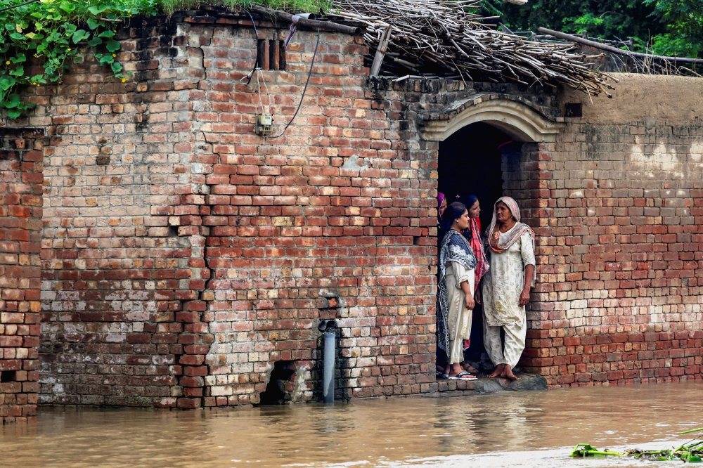 Residents stand at the entrance of a house on a flooded road, near the Pakistan-India border in Kasur district. — Reuters