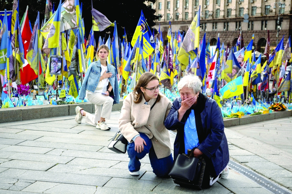 Bystanders take a knee to pay their respects to a fallen Ukrainian soldier, in Kyiv. — Reuters