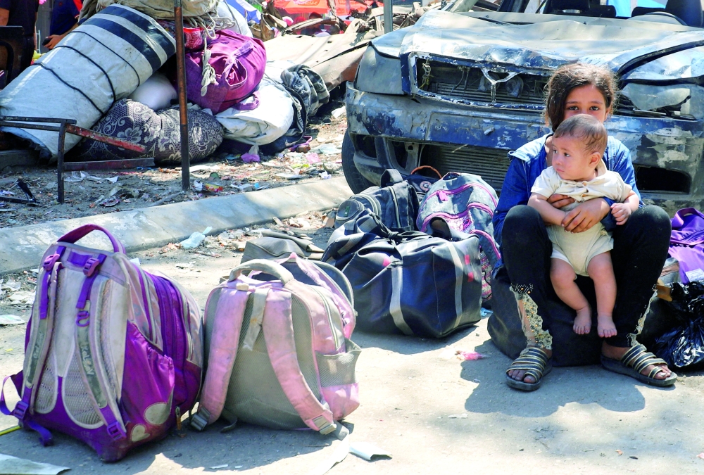 A Palestinian girl holds a child next to belongings, as displaced Palestinians flee amid an Israeli military operation, in Gaza. — Reuters