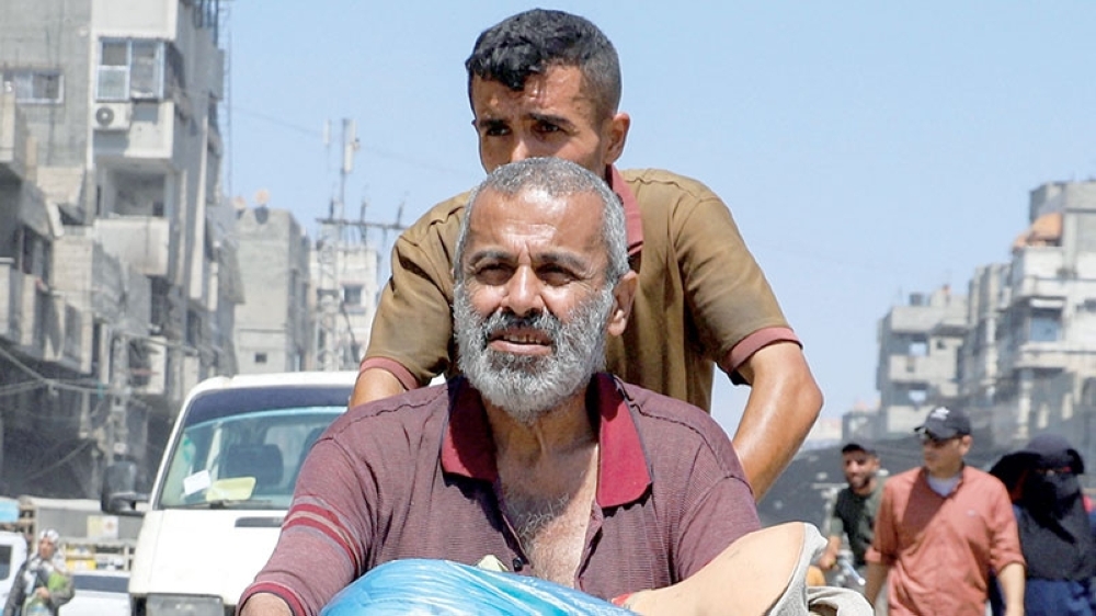 A displaced Palestinian man with amputated legs is pushed in a wheelchair while fleeing amid an Israeli military operation in Gaza City on Tuesday. - Reuters
