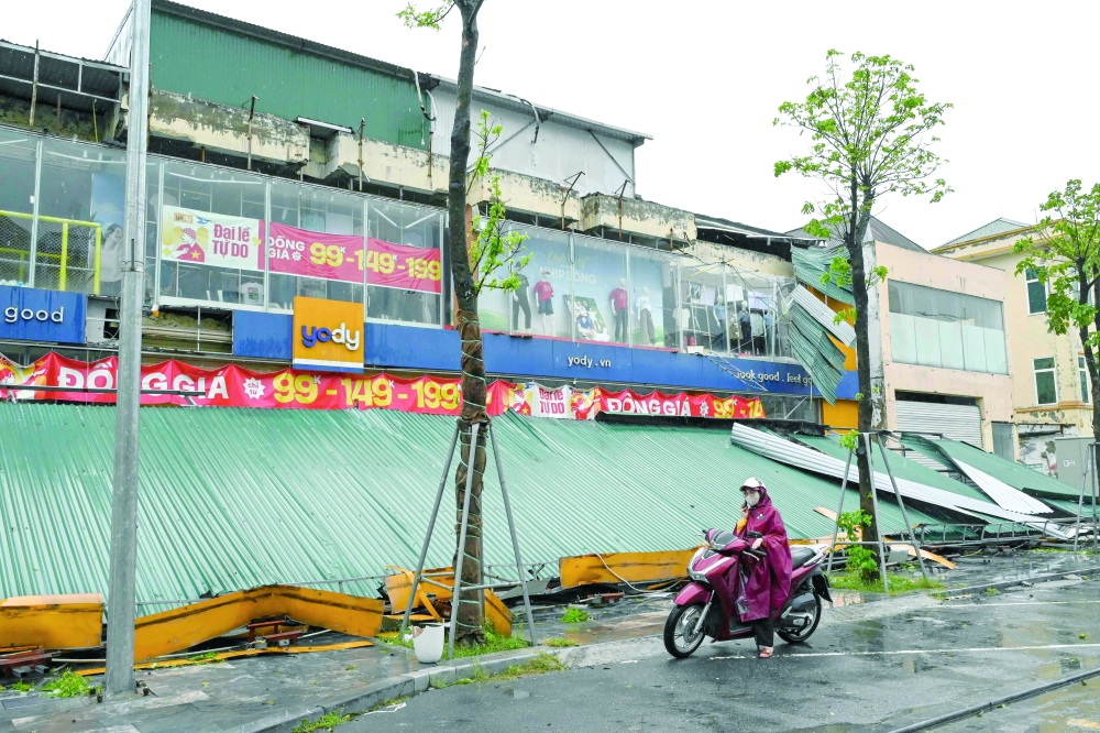 A woman stands next to a collapsed roof after Typhoon Kajiki passed, in Vietnam. — AFP