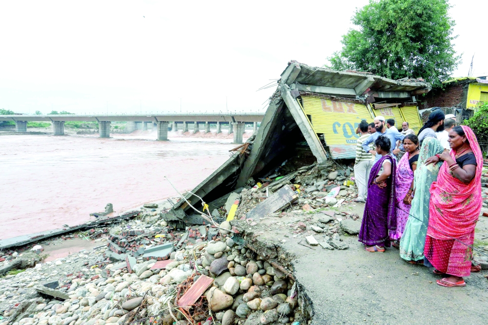 Onlookers gather near a damaged road along the banks of Tawi River, in Jammu. — AFP