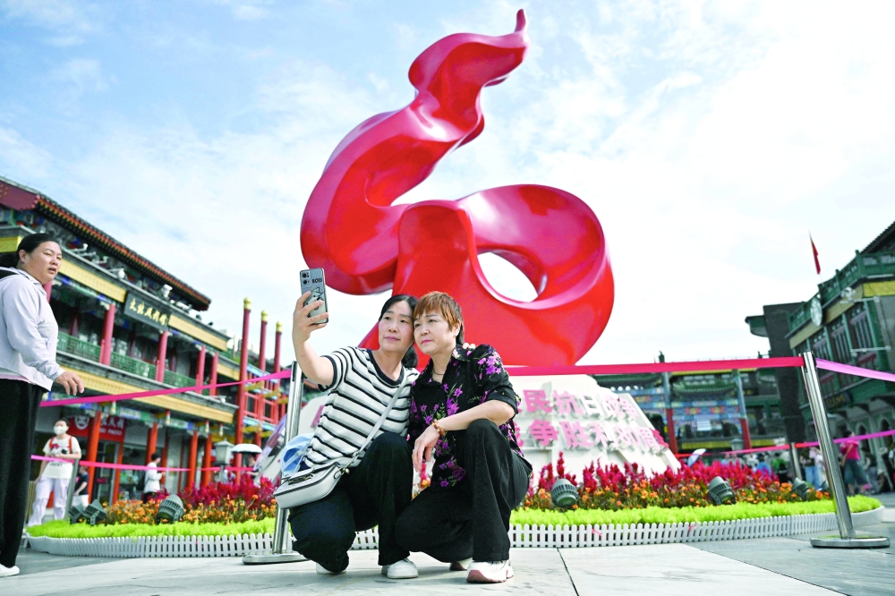 Two women take a selfie in front of a statue commemorating the 80th anniversary of victory over Japan and the end of World War II on Qianmen Street in Beijing. - AFP  