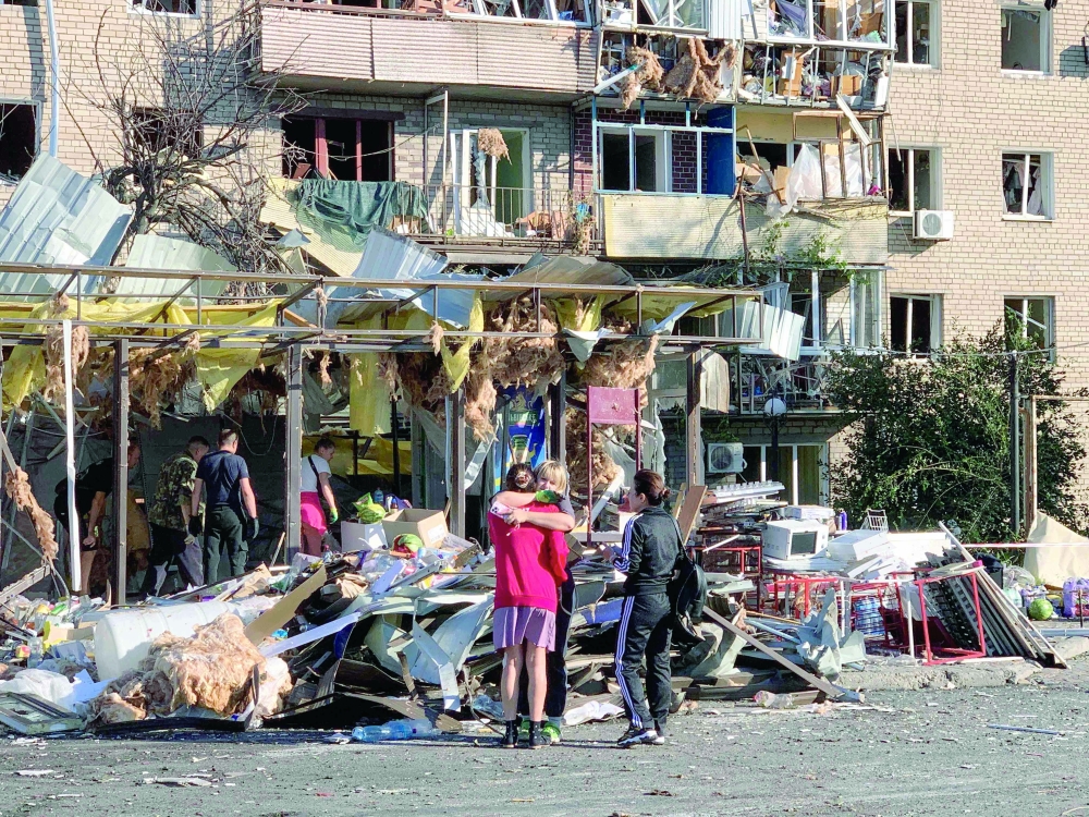 Local residents embrace each other next to a damaged residential building, in Zaporizhzhia. — AFP