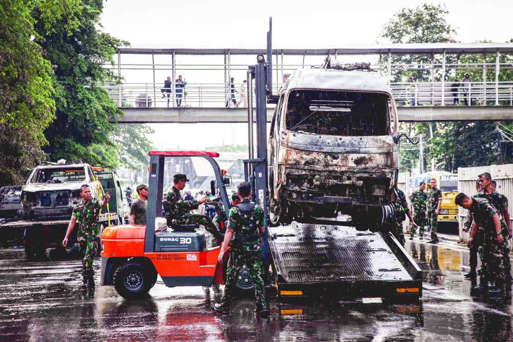 Indonesian army members load burned police vehicles, in Jakarta. — AFP