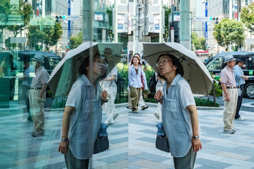 A woman with an umbrella walks in the scorching sun in Tokyo on September 1, 2025. (Photo by Philip FONG / AFP)
