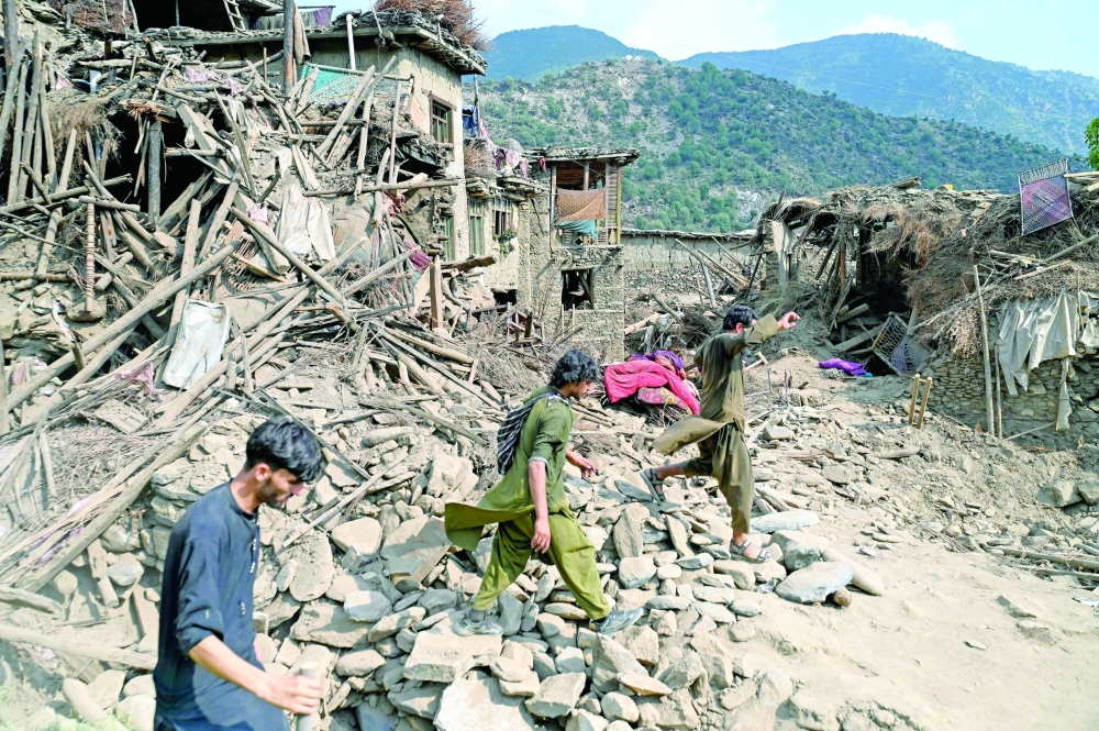 Afghans walk past damaged houses, in Kunar province, Eastern Afghanistan. — AFP