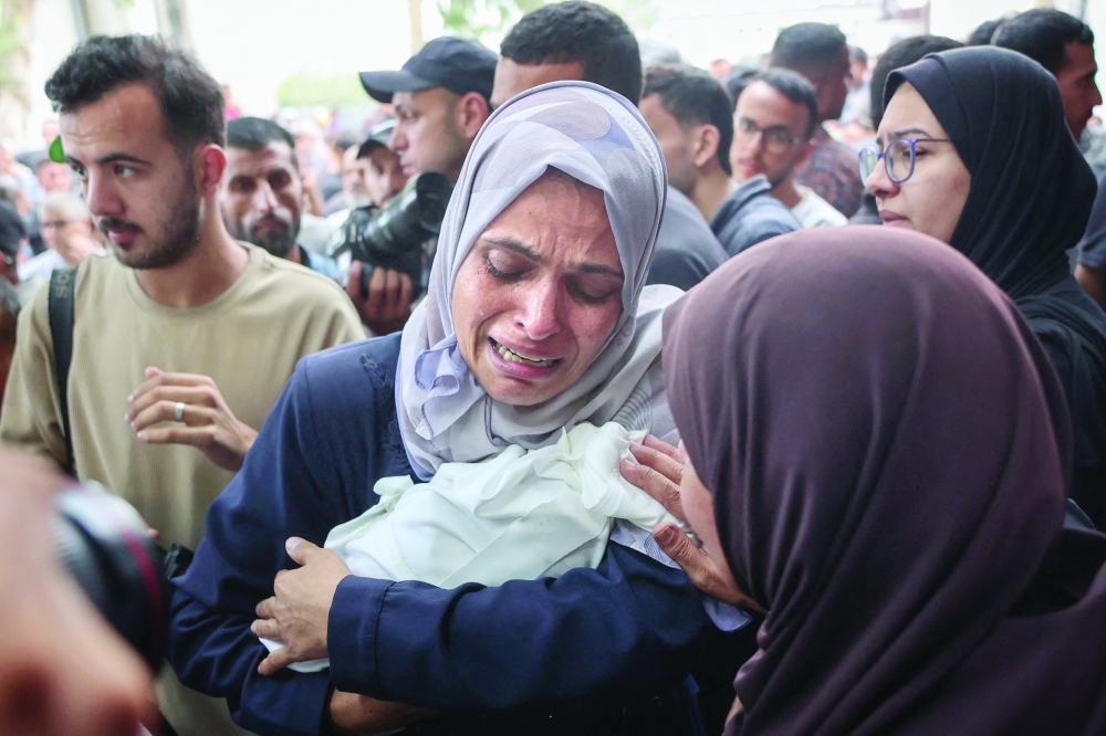 A Palestinian woman cries as she carries the body of a baby killed in Israeli strikes on Gaza City at dawn, before a funeral procession outside the Al Shifa Hospital. - AFP