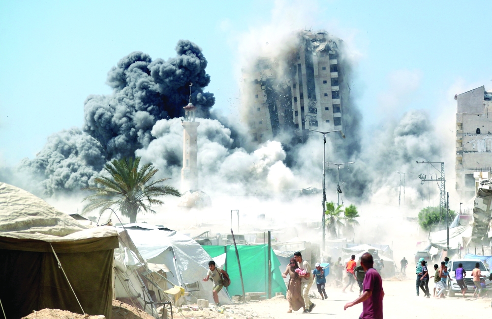 Palestinians run as a building hit by an Israeli air strike collapses in Gaza on Friday. — Reuters