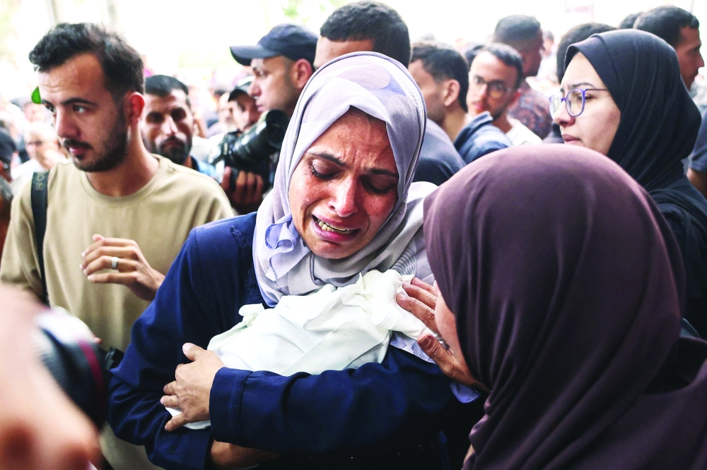 A Palestinian woman cries as she carries the body of a baby killed in Israeli strikes. — AFP