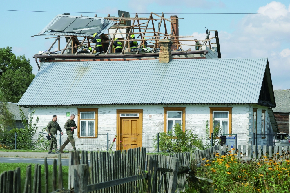 Polish soldiers walk below as firefighters work on the destroyed roof of a house, in Wyryki, Poland. — Reuters