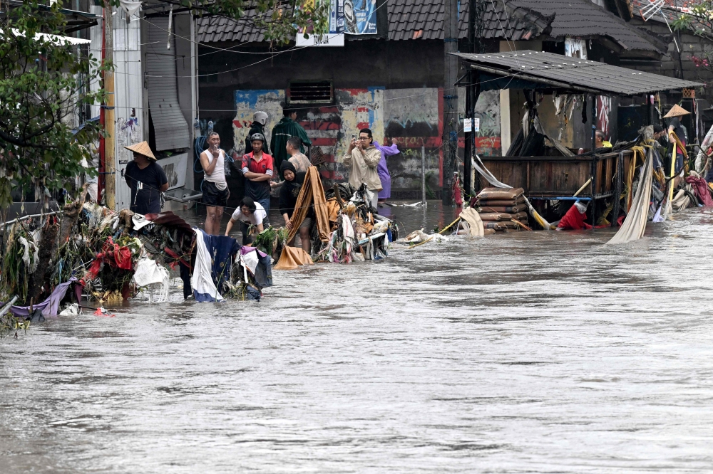 Flood-affected residents look on and clear debris in their neighbourhood following heavy rainfall in Denpasar