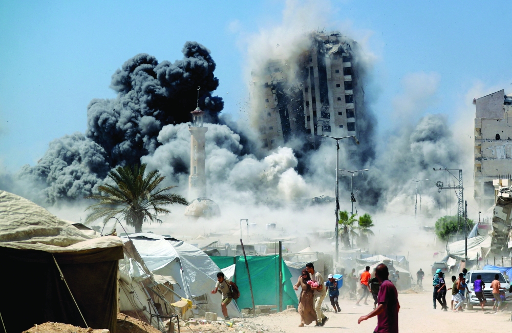 Palestinians run as the 15-storey Mushtaha Tower collapses after being hit by an Israeli air strike in Gaza City. - Reuters