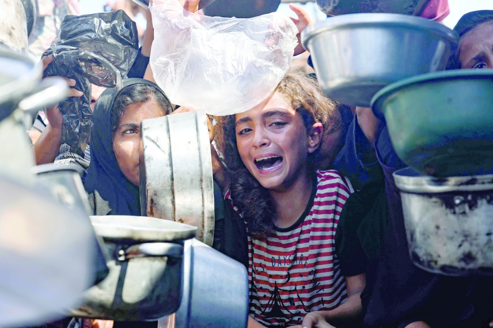 A young girl reacts as displaced Palestinians elbow their way in front of a community kitchen in Khan Yunis in the southern Gaza Strip. — AFP
