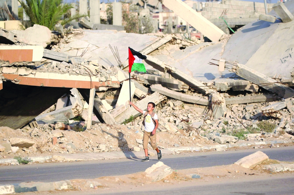 A displaced Palestinian child waves a Palestinian national flag as he walks past the rubble of a destroyed building at the Bureij camp for refugees in the central Gaza Strip on Monday. — AFP