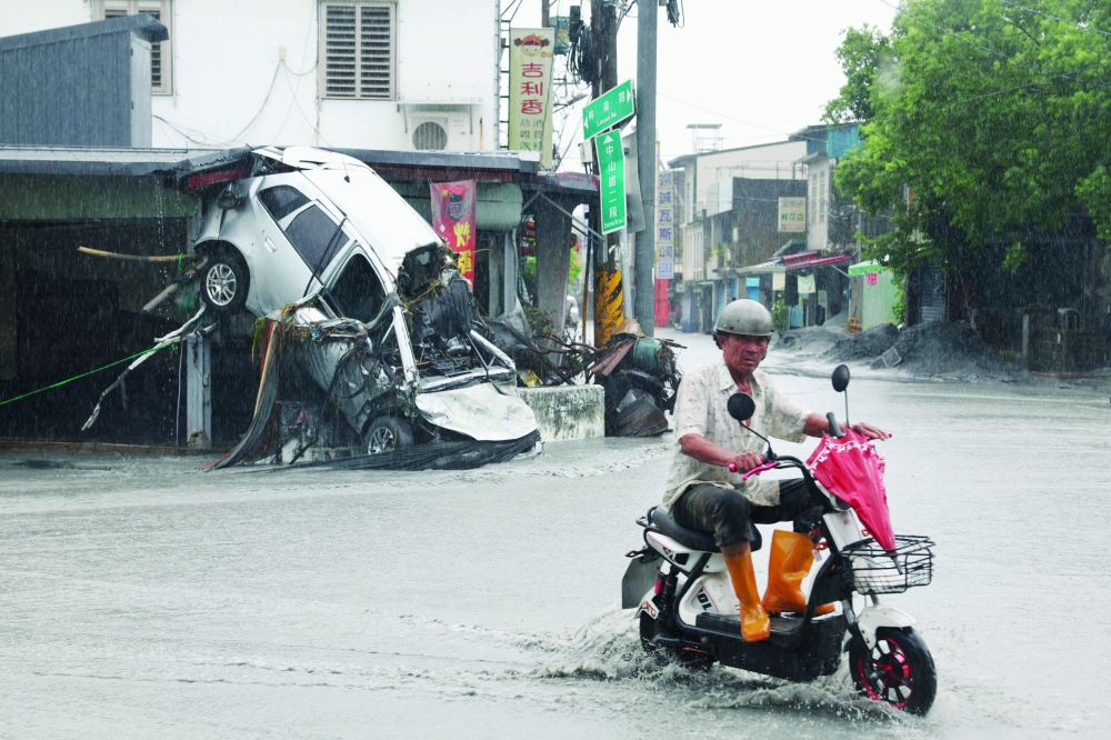A Guangfu village resident rides his scooter past a damaged car, in Hualien. — AFP