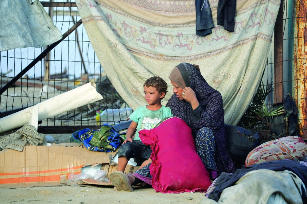 A Palestinian woman and a child who fled Gaza City sit near their belongings in the Nuseirat refugee camp. — AFP