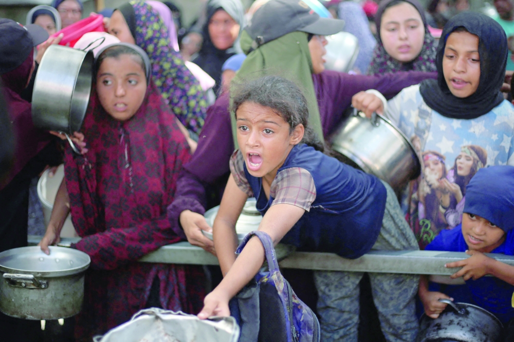 Palestinian children gather to receive food portions from a charity kitchen in Nuseirat, in the central Gaza Strip, on Tuesday. - AFP