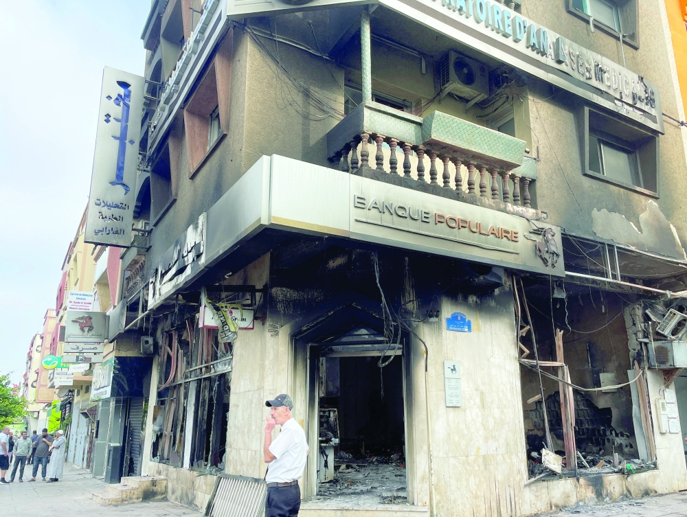 A man stands next to a burnt building which housed a bank, after youth-led anti-government protests, in Sale, Morocco. - Reuters 