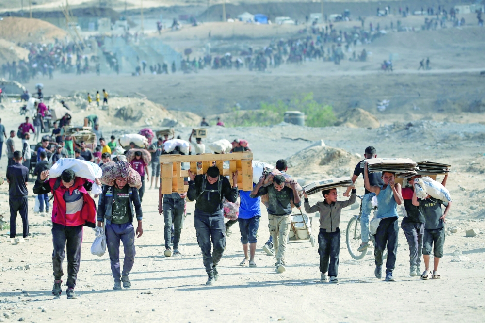 Palestinians carry bags, wooden pallets and empty cardboard boxes as they leave a food distribution point near the Netsarim corridor. — AFP
