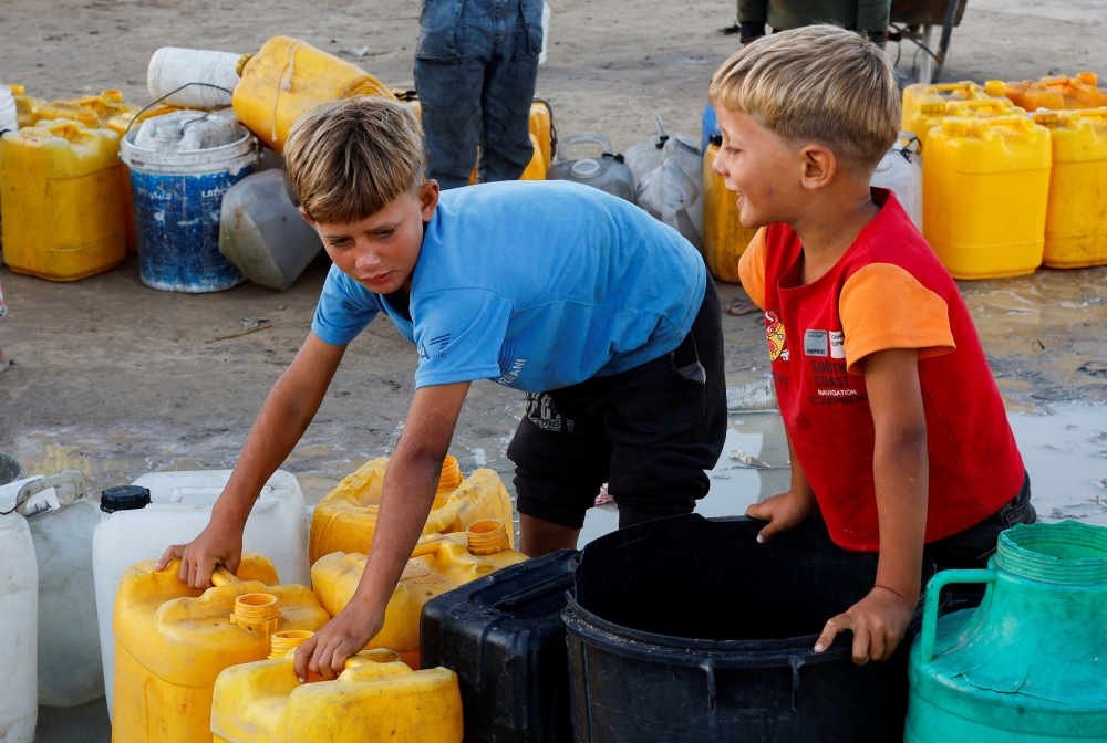 Displaced Palestinian children, who fled their homes due to the Israeli military offensive, wait to collect water in Nuseirat