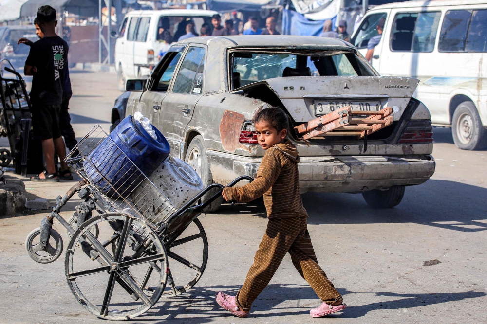  A girl pushes a broken wheelchair loaded with jerrycans along a road at a camp for people displaced by war in northern Nuseirat in the central Gaza Strip