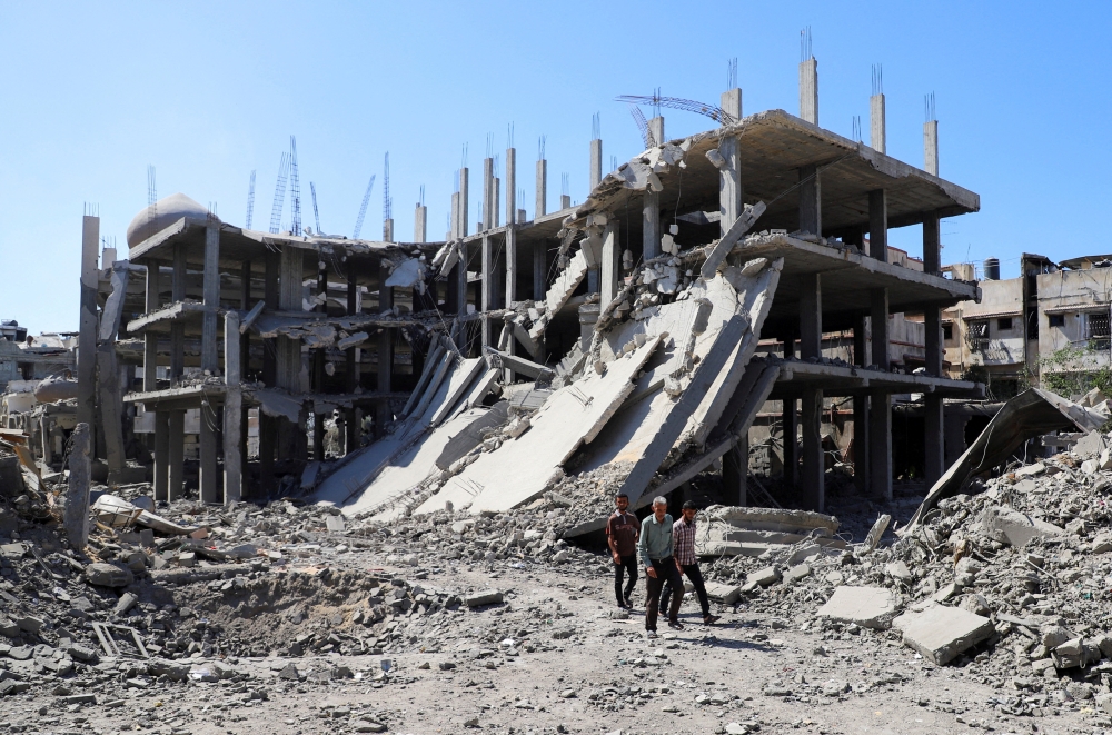 Palestinians walk past a destroyed building, as they inspect the damage in the aftermath of Israeli operation at Sabra neighbourhood in Gaza City