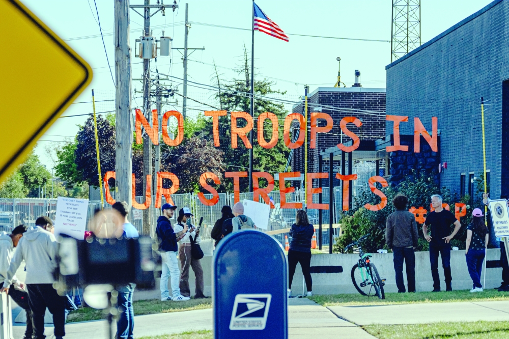 Demonstrators and members of the media near a “No Troops in Our Streets” sign outside an immigrant processing and detention center in Broadview. 