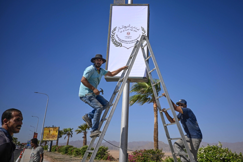 Municipal workers hang a sign near the airport in Sharm el-Sheikh, as the Egyptian Red Sea resort prepares to host a US-brokered international Gaza peace summit