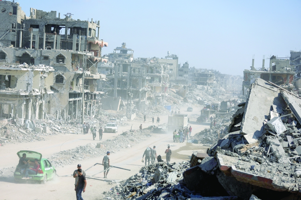 Palestinians walk past the rubble of destroyed buildings in Gaza City on Thursday. — Reuters