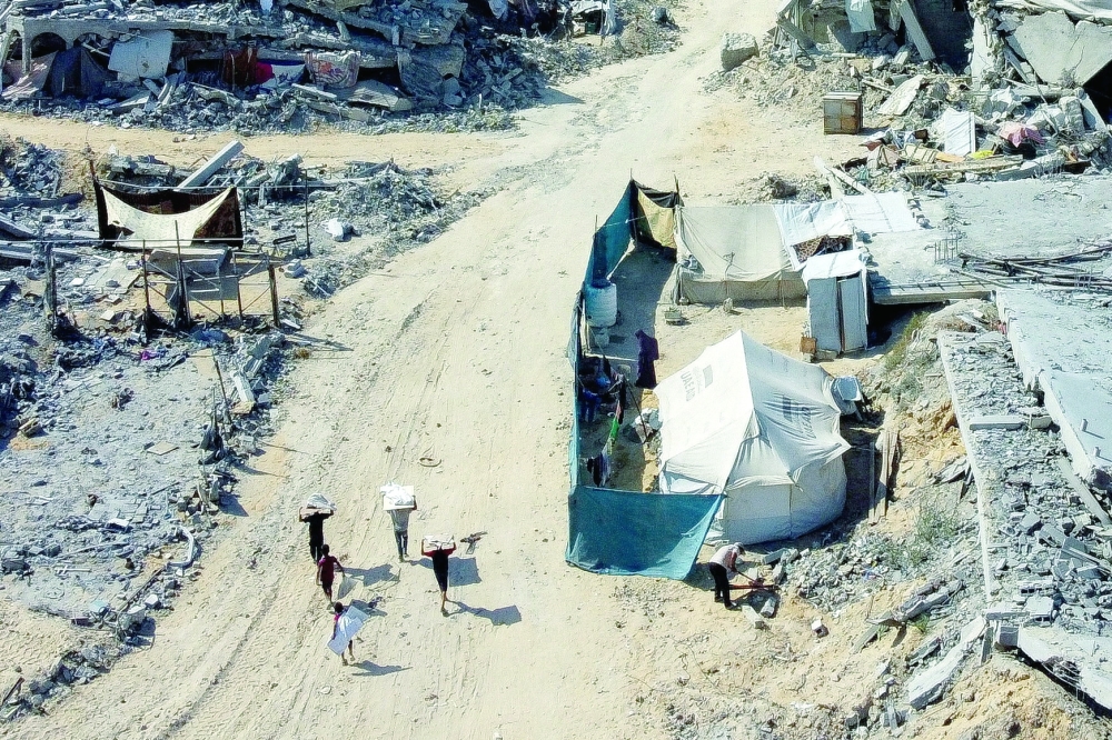 Palestinians walk past a tent amid the rubble in a destroyed area, in Gaza City. — Reuters