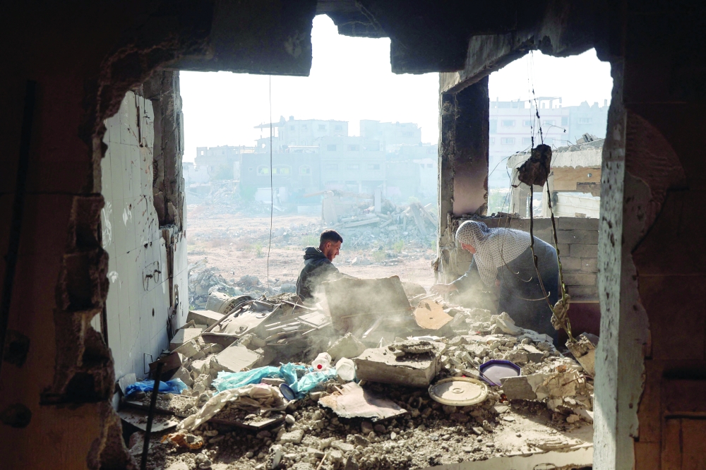 A displaced Palestinian woman swifts through debris with her grandson upon returning to her home, which was heavily damaged by Israeli bombardments in the Bureij refugee camp. — AFP
