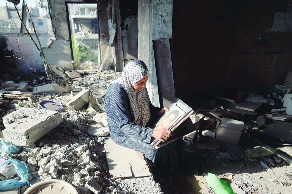 Umm Jameela Abdul-Razzaq looks at a portrait of her father as she sits amid debris upon returning to her home, which was heavily damaged by Israeli bombardments in the Bureij refugee camp. — AFP