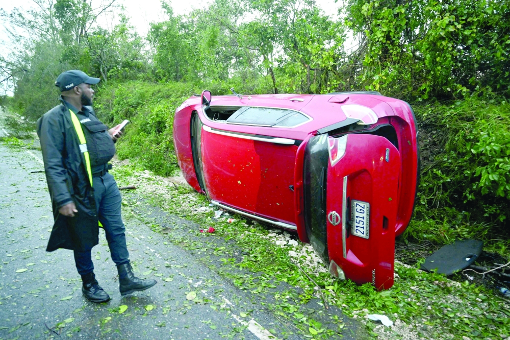 A police officer inspects a car damaged by a fallen tree after the passage of Hurricane Melissa in Manchester, Jamaica, on Wednesday. — AFP