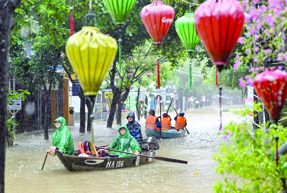 People navigate a flooded street on boats during heavy rains in Hoi An. - AFP