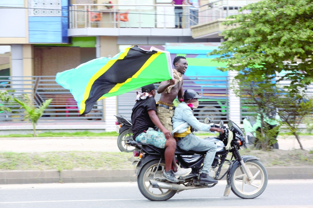 People ride on a motorcycle waving a Tanzanian flag during violent protests that marred the election following the disqualification of the two leading opposition candidates in Dar es Salaam. — Reuters