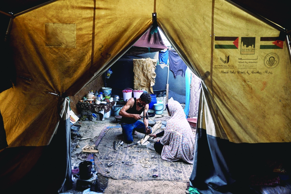A man and a woman chip wood inside a tent at a makeshift shelter in Gaza City on November 3, 2025, during a ceasefire in the two-year-long Israel-Hamas war.  (Photo by Omar AL-QATTAA / AFP)