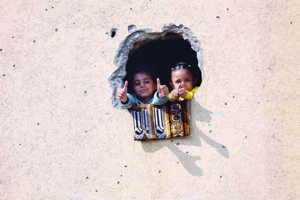 Children look through a hole in a wall during an exhibition featuring a collection of drawings by children and women reflecting feelings of loss and hope, at a school-turned-shelter for displaced Palestinians in Al Rimal neighbourhood of Gaza City on Wednesday. - AFP