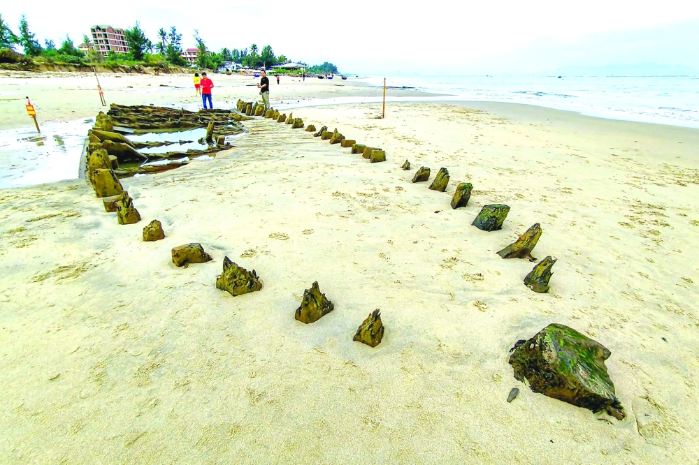 People stand next to a centuries-old shipwreck uncovered in the aftermath of Typhoon Kalmaegi on a beach off the Hoi An coast in central Vietnam. — AFP