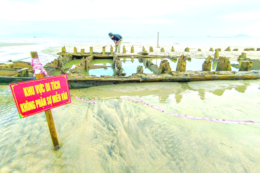 A man examines a centuries-old shipwreck uncovered in the aftermath of Typhoon Kalmaegi on a beach off the Hoi An coast in central Vietnam. — AFP